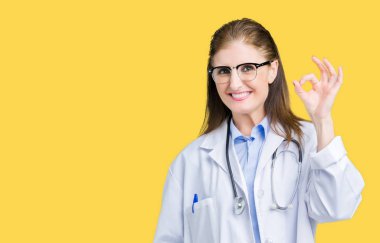 Orta yaş olgun doktor kadın izole arka plan el ve parmaklar ok işaretiyle yapıyor olumlu gülümseyen üzerinde tıbbi bir palto giyiyor. Başarılı ifade.