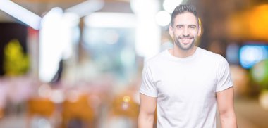 Yüzünde mutlu ve güzel bir gülümseme ile izole arka plan üzerinde giyen casual beyaz t-shirt genç adam. Şanslı kişi.