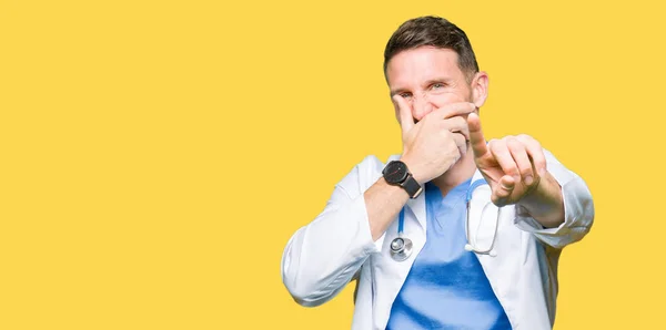 Handsome doctor man wearing medical uniform over isolated background Laughing of you, pointing to the camera with finger hand over mouth, shame expression