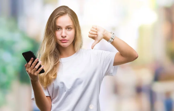 年轻美丽的金发碧眼的女人使用智能手机在孤立的背景与愤怒的脸 负面的迹象显示不喜欢大拇指下来 拒绝的概念 — 图库照片