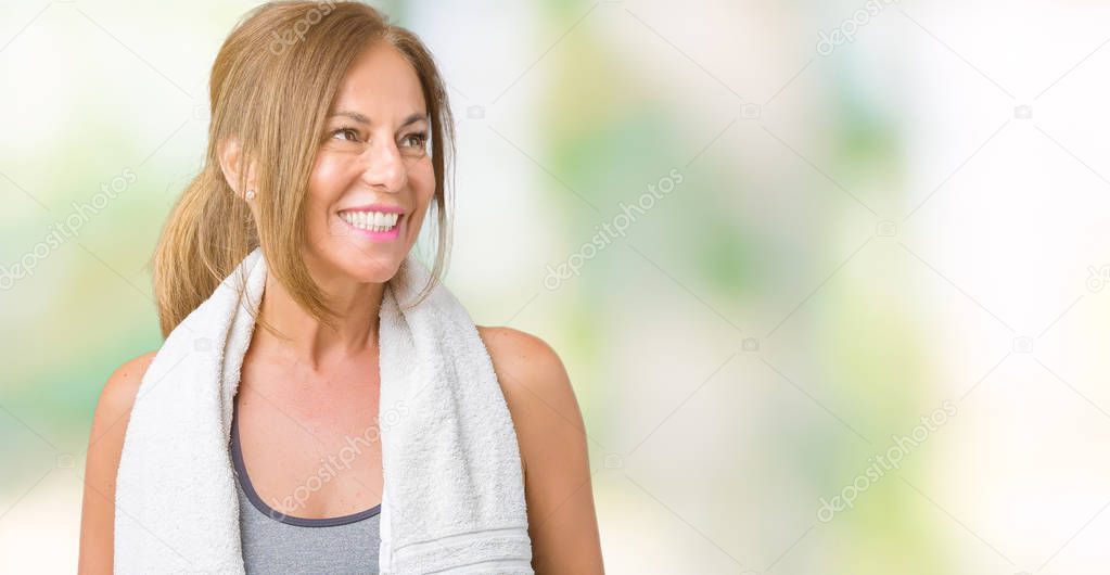 Beautiful middle age woman wearing sport clothes and a towel over isolated background looking away to side with smile on face, natural expression. Laughing confident.