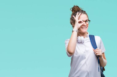 Gülümseyerek el parmakları ile mutlu yüz üzerinden seyir göz ile ok jest yapıyor izole arka plan üzerinde sırt çantası ve kulaklıklar giyen genç esmer öğrenci kız.