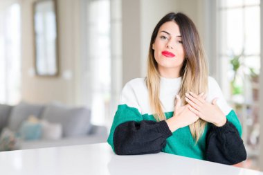 Göğüs kapalı gözlerle ellerinde ve yüzünde minnettar jest ile evde kış kazak giyen genç güzel kadın gülümsüyor. Sağlık kavramı.