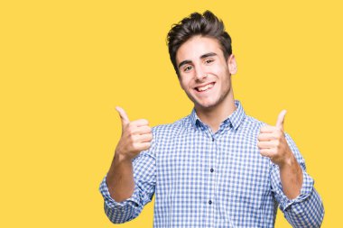 Genç yakışıklı iş adamı izole arka plan başarı işareti el ile pozitif jest yapıyor üzerinde başparmak gülümseyen ve mutlu. Neşeli bir ifadeyle, kazanan jest kameraya bakıyor.