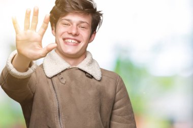 Gösterilen arka plan üzerinde kış ceket giyen genç yakışıklı adam izole ve parmakları ile işaret kendinden emin ve mutlu gülümseyerek süre beş numara.