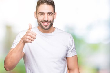 Hareketi el ile mutlu yaşasın yapıyor izole arka plan üzerinde rahat beyaz t-shirt giyen genç adam. Başarı gösteren kameraya bakarak ifade onaylama.