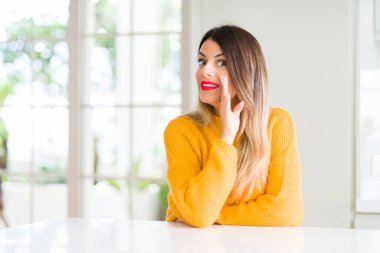 Genç güzel kadın giyiyor kış kazak evde el gizli söylenti, kötü niyetli konuşma konuşma fısıldayarak söylemek dudaklarından