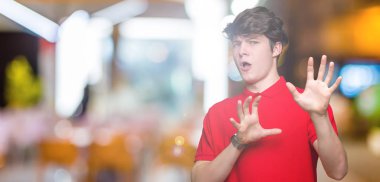 Şokta bağırarak korkuyor ve dehşet korku ifade dur hareketi el ile ile izole arka plan üzerinde kırmızı t-shirt giyen genç yakışıklı adam. Panik kavramı.