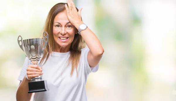 Middle age hispanic winner woman celebrating award holding trophy over isolated background stressed with hand on head, shocked with shame and surprise face, angry and frustrated. Fear and upset for mistake.