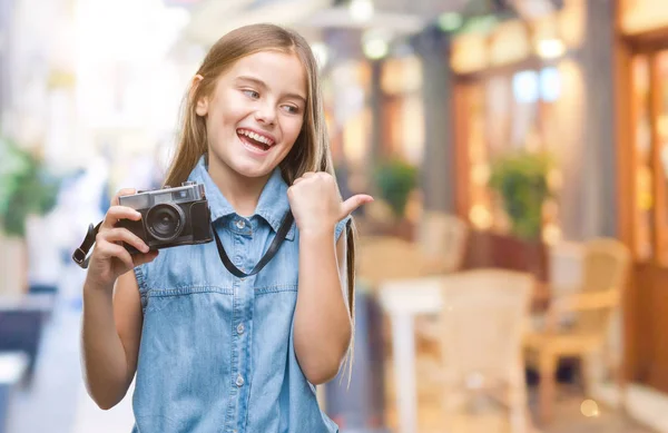 年轻美丽的女孩拍照使用老式相机在孤立的背景指向和显示与快乐的脸微笑的一侧与拇指 — 图库照片