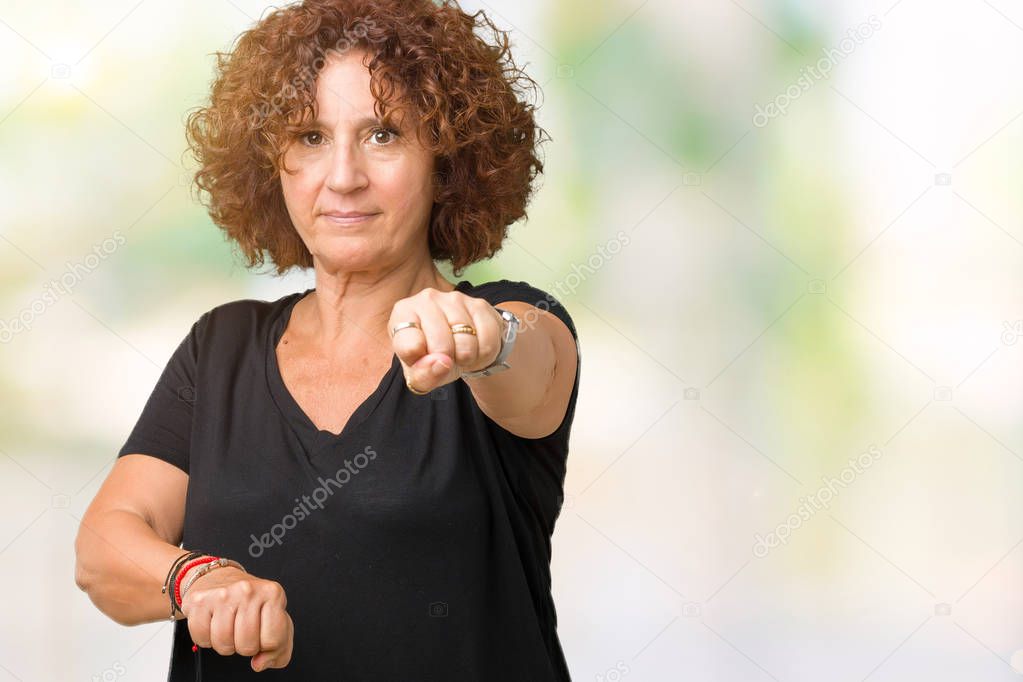 Beautiful middle ager senior woman over isolated background Punching fist to fight, aggressive and angry attack, threat and violence