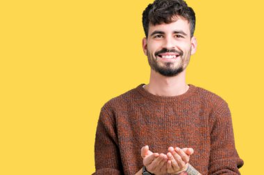 Genç yakışıklı adam giyen kış kazak izole üzerinden alma veya jest vererek birlikte el avuç içi ile gülen arka plan. Ayrı tutma ve koruma