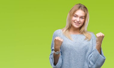 Üzerinde kış kazak giyen genç beyaz kadın gülümseyerek ve başarı için çığlık arka plan çok mutlu ve heyecanlı kaldırdı, silah ile kazanan jest yapıyor izole. Kutlama kavramı.