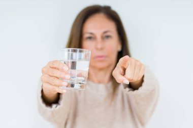 Orta yaş kadın içme cam izole su arka kamera ve size parmak ile işaret, el işareti, pozitif ve kendinden emin bir jest ön