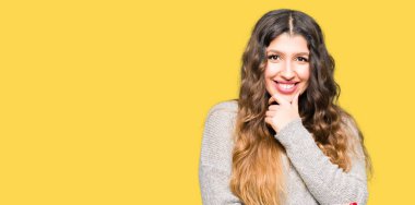 Emin çapraz kollar ve çeneme kaldırdı el ile gülümseme ile kameraya bakarak kış elbise giyen genç güzel kadın. Pozitif düşünce.