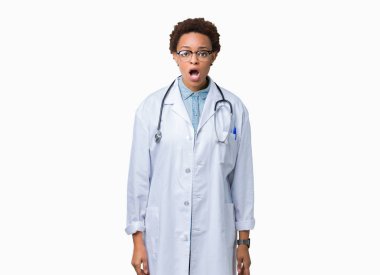 Genç Afro-Amerikan doktor kadın giyiyor tıbbi kat izole arka plan korkuyor ve şok sürpriz ifade ile üzerinde korku ve yüz heyecanlı.