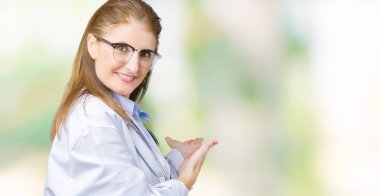 Orta yaş olgun doktor kadın izole arka plan açık el ile doğal gülümseyen girmek için davet üzerinde tıbbi bir palto giyiyor
