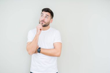 Çene düşünme hakkında soru, dalgın ifade üzerine el ile izole arka plan üzerinde rahat beyaz t-shirt giyen genç yakışıklı adam. Düşünceli yüzüyle gülümsüyor. Şüphe kavramı.