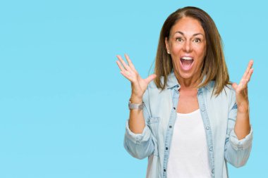 Orta yaş yetişkin kadın üzerinde rahat kot gömlek giymiş deli kutluyor arka plan izole ve başarı için kaldırdı kollarını açarak hayrete ve heyecanlı çığlık gözleri açık. Kazanan kavramı