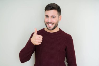 Genç yakışıklı adam hareketi el ile mutlu yaşasın yapıyor izole arka plan üzerinde bir kazak giyiyor. Başarı gösteren kameraya bakarak ifade onaylama.