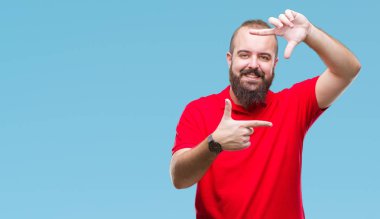 Elle yapma çerçeve ve parmakları ile mutlu yüz gülümseyen izole arka plan üzerinde kırmızı gömlek giymiş genç beyaz hipster adam. Yaratıcılık ve Fotoğrafçılık kavramı.