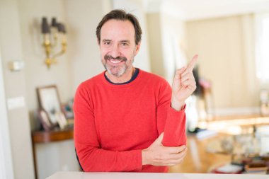 Kameraya bakarak yan el ve parmak ile işaret eden yakışıklı orta yaş erkek evde yüzünde kocaman bir gülümseme ile.
