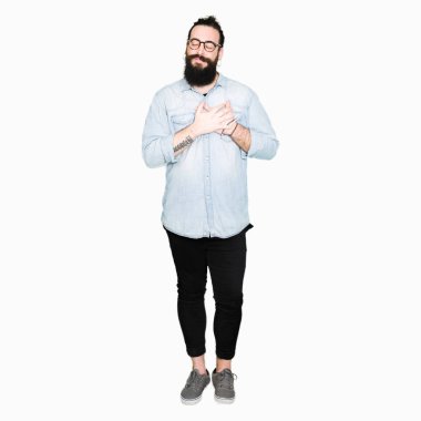 Uzun saç ve sakal ile gülümseyen gözlüklü genç hipster adamla kapalı gözler ve yüzünde minnettar jest ile göğüs üzerinde eller. Sağlık kavramı.