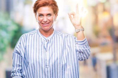 Atrractive üst düzey beyaz Kızıl saçlı kadın izole arka plan el ve parmaklar ok işaretiyle yapıyor olumlu gülümseyen üzerinde. Başarılı ifade.