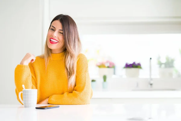 Young beautiful woman drinking a cup of coffee at home winking looking at the camera with sexy expression, cheerful and happy face.