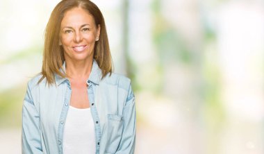 Orta yaş yetişkin kadın yüzünde mutlu ve güzel bir gülümseme ile izole arka plan üzerinde rahat kot gömlek giymiş. Şanslı kişi.