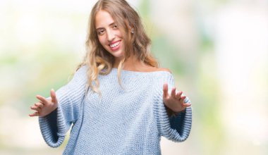 Sarılmak için kollarını açarak gülümseyerek kameraya bakarak izole arka plan üzerinde kış kazak giyen güzel genç sarışın kadın. Neşeli ifade kucaklayan mutluluk.