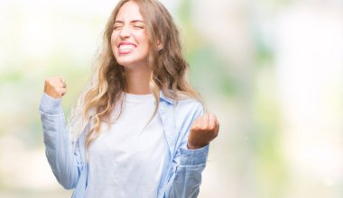 Gülümseyen ve başarı için çığlık güzel sarışın genç kadın üzerinde izole arka plan çok mutlu ve heyecanlı kaldırdı, silah ile kazanan jest yapıyor. Kutlama kavramı.