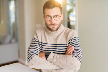 Yakışıklı delikanlı giymiş evde şüpheci ve sinir, onaylamayan ifade yüz çapraz kolları üzerinde gözlük. Negatif kişi.