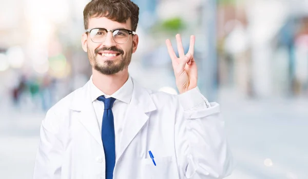 年轻的专业科学家男子穿着白色外套在孤立的背景显示和手指第三 同时微笑着自信和快乐 — 图库照片