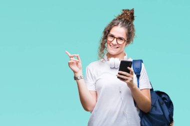 Sırt çantası, kulaklık ve smartphone izole arka tarafına el ve parmak ile işaret çok mutlu üzerinde giyen genç esmer öğrenci kız