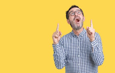 Yakışıklı orta yaş zarif üst düzey iş adamı izole arka plan üzerinde gözlük hayrete ve yukarıya bakıyor ve parmakları ile işaret ve silah kaldırdı şaşırttı.