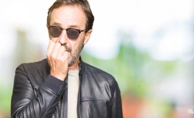 Orta yaş yakışıklı adam güneş gözlüğü ve stresli ve gergin ile seyir siyah deri ceket giyen tırnak ısırma dudaklarından eller. Anksiyete sorunu.