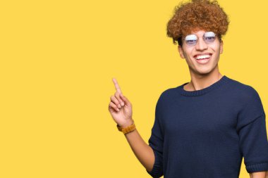 Gözlüklü kocaman bir gülümseme ile yüzünde, afro kameraya bakarak yan el ve parmak ile işaret eden genç yakışıklı adamla.