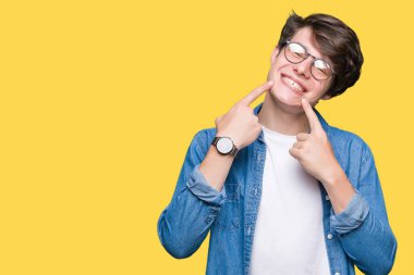 Kendinden emin gösterilen ve işaret parmakları diş ve ağız ile gülümseyen izole arka plan üzerinde gözlük takan yakışıklı delikanlı. Sağlık kavramı.