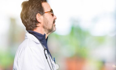 Yakışıklı orta yaş doktor erkek tarafına, seyir tıbbi bir palto giyiyor dinlenmek doğal yüz emin gülümseme ile pozuyla profili.
