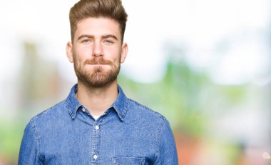 Komik surat ile yanakları şişirme rahat kot gömlek giymiş genç yakışıklı sarışın adam. Ağız ile hava, deli ifade şişirilmiş.