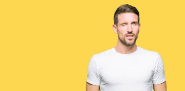 Casual beyaz t-shirt seksi bir ifadeyle, neşeli ve mutlu yüzünü kameraya bakarak göz kırpıyor giyen yakışıklı adam.