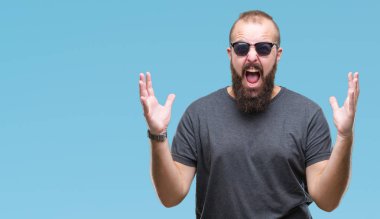 Üzerinde güneş gözlüğü takmış Genç beyaz hipster adam arka plan deli izole ve deli bağırarak ve agresif ifade ve silah kaldırdı bağırıyor. Hayal kırıklığı kavramı.