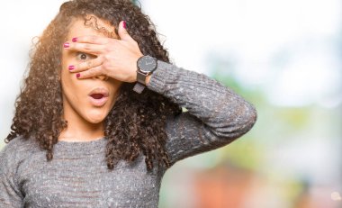 Yüz ve gözler el ile kapsayan şok gri kazak bakmak giyen kıvırcık saçlı Genç güzel kadın mahcup ifadeyle parmaklarımın arasından arıyor.