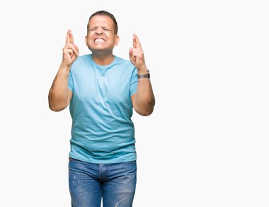 Orta yaş Arap adam geçiş parmakları umut ve gözleri kapalı ile gülümseyen izole arka plan üzerinde mavi tişört giyiyor. Şans ve batıl kavramı.