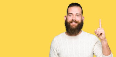 Kış kazak gösterme ve kendinden emin ve mutlu gülümseyen bir parmak ile işaret eden oktan yukarı giyen genç hipster adam.