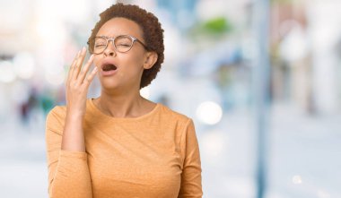 Genç güzel Afrikalı-Amerikalı kadın izole arka plan üzerinde gözlük el ağzıyla kapsayan yorgun esneme sıkılmış. Restless ve uyku hali.