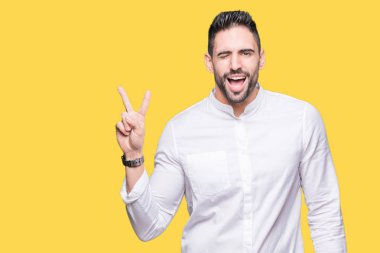 Mutlu yüz zafer işareti yaparken kameraya göz kırpıyor ile gülümseyen izole arka plan üzerinde genç iş adamı. İki numaralı.