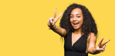 Kıvırcık saçlı giyen moda etek kamera zafer işareti yapıyor parmak gösteren seyir gülümseyen genç güzel kız. İki numaralı.