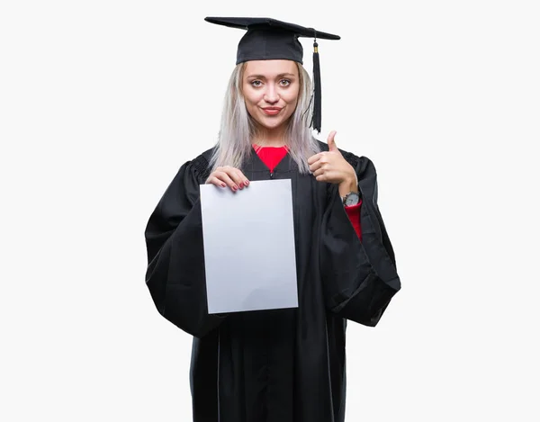 笑顔の サイン 優秀な兆候を親指をやって幸せな孤立の背景の上の学位を保持研究科の制服を身に着けている若いブロンドの女性 — ストック写真